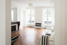 a chic living room with white walls and a rich stained parquet floor, white and black furniture and a refined fireplace
