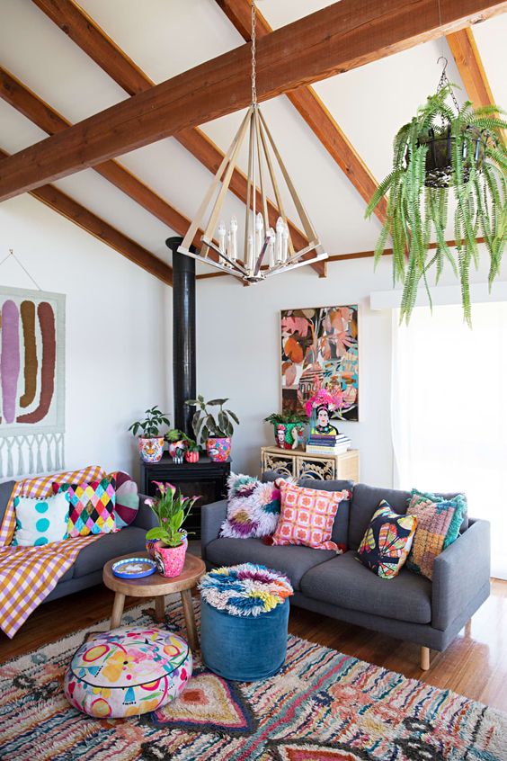 a colorful boho living room with grey sofas, colorful textiles, bold ottomans, a pendant greenery piece and artworks