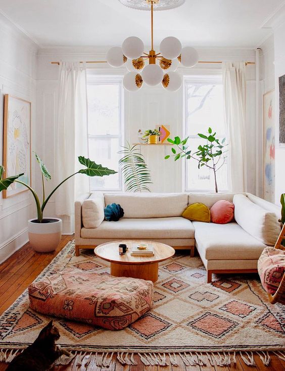 a colorful summer living room with a white sectional, a boho rug and a pouf, a round coffee table, potted plants