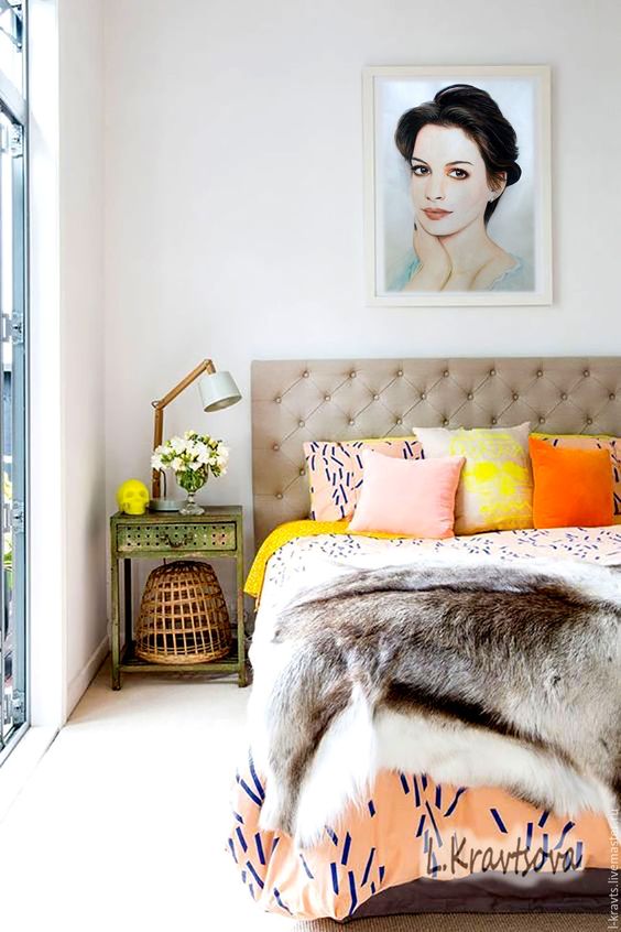 a cool summer bedroom with a grey upholstered bed, colorful printed bedding, a vintage nightstand and a cool lamp