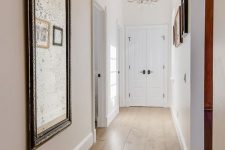 a corridor with white walls and a bamboo floor, a gallery wall and a mirror in a vintage frame plus a crystal chandelier