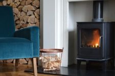 a cozy fireplace nook with lovely parquet floors, a hearth, a navy chair, some firewood stored and a basket