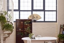 a creative bathroom with white brick walls and a cork wall, a vintage tub, a stand and a dark stained storage unit and potted plants