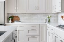 a dove grey farmhouse kitchen with a rich-stained laminate floor, a marble subway tile backsplash and white countertops