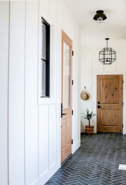 a farmhouse entryway with white paneled walls and a navy chevrong tile floor, wooden doors and pendant lamps
