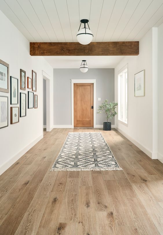 a farmhouse entryway with white walls, vinyl flooring that looks like laminate, a wooden beam on the ceiling, a rug and a gallery wall