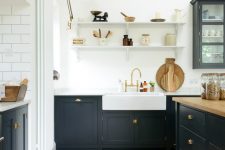 a farmhouse kitchen with white walls and a parquet floor, dark grey cabinets, butcherblock countertops and brass touches