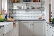 a grey Scandi attic kitchen with white subway tiles, black stone countertops, open shelves and neutral knobs is chic