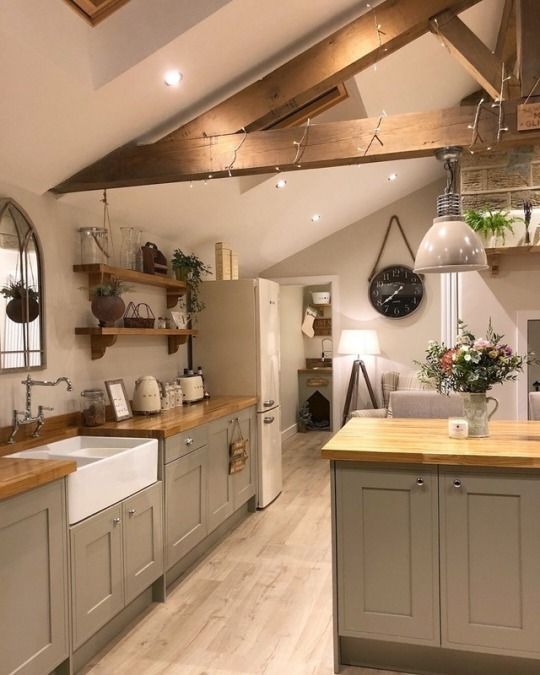 a grey farmhouse attic kitchen with butcherblock countertops, open shelves and wooden beams, a mirror and a vintage faucet