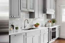 a grey farmhouse kitchen with shaker-style cabinets, a dark laminate floor, a white tile backsplash and neutral fixtures