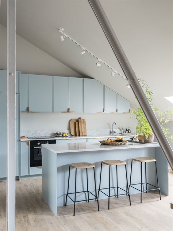 a light blue attic kitchen with sleek cabinets and a kitchen island, a skylight, a potted plant and stools is chic