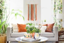 a lively summer living room with a grey sofa, bold pillows and bold printed curtains, a fringe decoration and lot sof plants