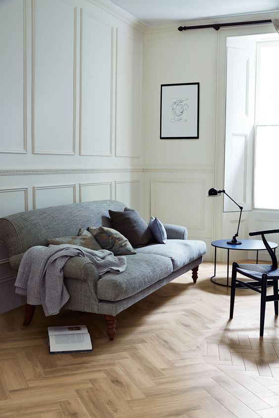 a lovely Nordic living room with creamy panels on the walls, light stained parquet flooring, a grey sofa, black chairs and a table