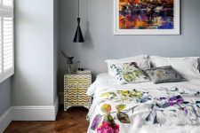 a lovely bedroom with grey walls, a dark stained parquet floor, chic furniture with floral bedding and a bold watercolor artwork