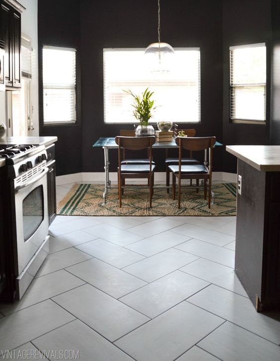 a lovely eat-in kitchen with a tile floor and black walls, dark cabinetry, lovely leather chairs and a metal dining table