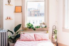 a lovely summer bedroom with tall windows, mini shelves with various decor, a bed with pink bedding and lots of plants
