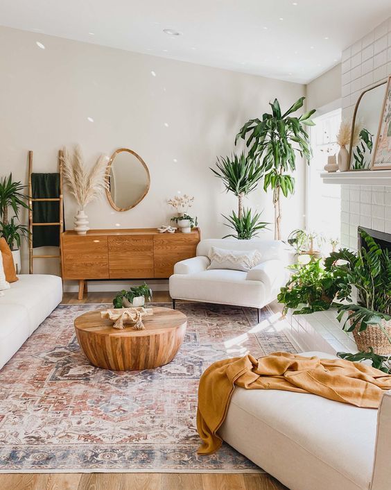 a lovely summer living room with white furniture, warm earthy textiles, potted plants, a fireplace and a wooden coffee table