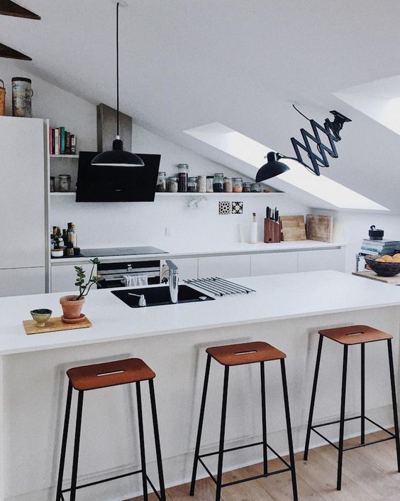 a minimalist attic kitchen with sleek cabinetry, tall stools, skylights, black fixtures looks very stylish and bold