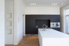 a minimalist kitchen with black cabinetry, a white kitchen island and a parquet floor plus built-in lights is chic