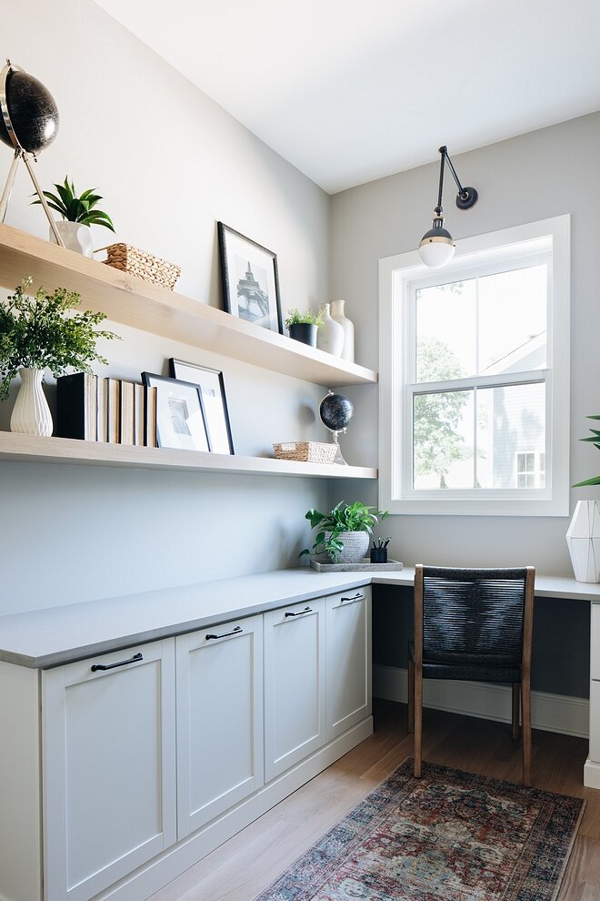 a modern and neutral coastal home office in light grey, with shaker-style cabinets, floating shelves, a built-in desk and a black chair