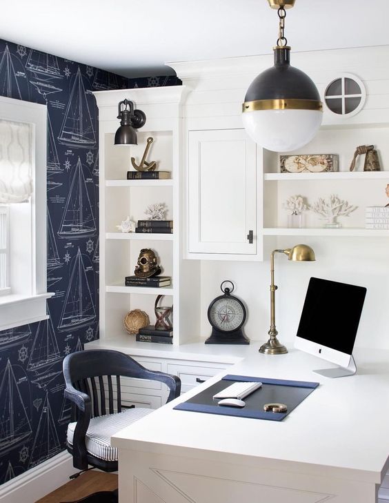 a modern coastal or nautical home office with a navy accent wall, a white storage unit with a desk, a navy chair and bold sea-inspired decor