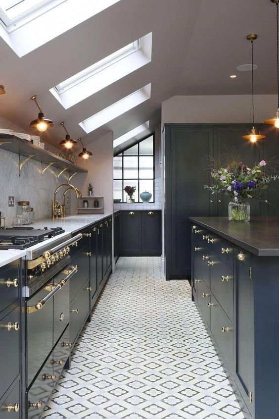 a navy attic kitchen with elegant gold touches, sconces and pendant lamps and lots of skylights to brign more light in
