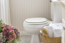 a neutral bathroom with white planked walls, a grey printed vinyl floor, white furniture and appliances and some blooms