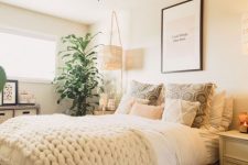 a neutral boho summer bedroom with wooden furniture, printed and knit and crochet bedding, a macrame lamp and lots of greenery