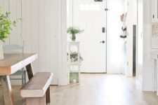 a neutral farmhouse space with laminate flooring, white walls, wooden furniture, potted plants and a pendant lamp