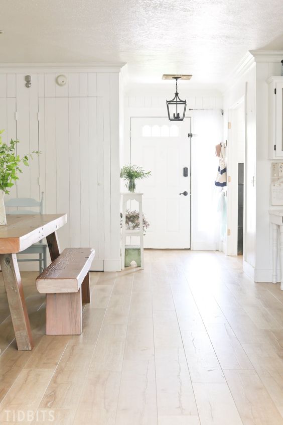 a neutral farmhouse space with laminate flooring, white walls, wooden furniture, potted plants and a pendant lamp