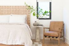a neutral summer bedroom with a wooden bed with a leather headboard and a leather chair, neutral textiles and greenery in a vase
