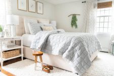 a neutral summer sleeping space with an upholstered bed, blue bedding, white nightstands, a gallery wall and greenery