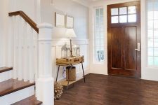 a rustic entryway with a vinyl floor that imitates stained wood, a matching door, a suitcase console table and pretty lamps