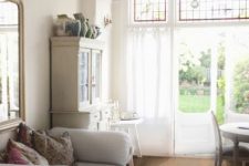 a shabby chic living and dining room with bamboo floors, white and neutral furniture, a crystal chandelier, a glazed wall with an entrance to the garden