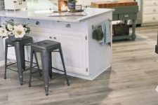 a simple farmhouse kitchen with a vinyl floor, white cabinets, a grey subway tile backsplash, metal stools and a green kitchen island