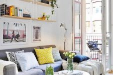 a small and bright summer living room with a grey sofa, round tables, open shelves and bright textiles
