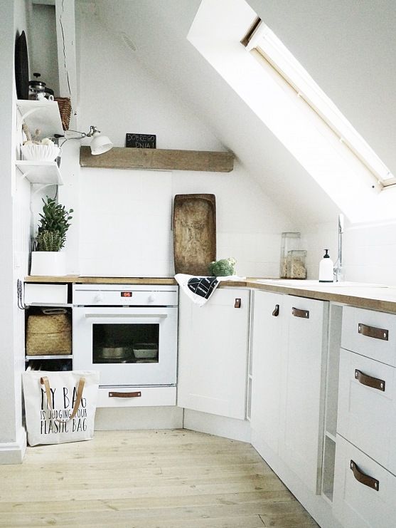 a small and neutral attic kitchen with white cabinetry and leather pulls, butcherblock countertops and a wooden slab shelf