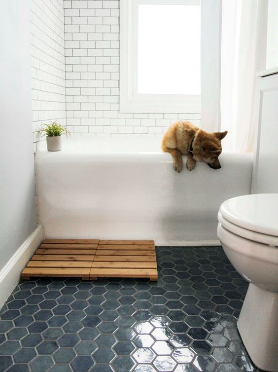 a small bathroom with white subway tiles and navy hexagon ones on the floor, a wooden bathmat and a potted plant is very cool