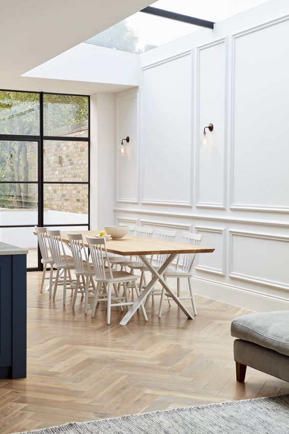a sophisticated dining room with a trestle table, white chairs, creamy panels on the walls and a skylight