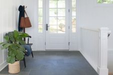 a stylish and airy entryway with a tile and laminate floor, a small black bench and a potted plant plus a pendant lamp