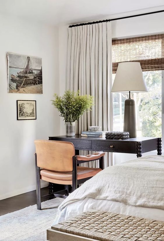 a stylish bedroom done in neutrals, with a black desk and a leather chair for working placed by the window