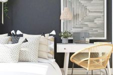 a stylish bedroom with black walls, white furniture, a rattan chair, an abstract artwork is an office bedroom combo