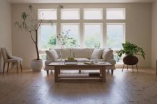 a stylish contemporary living room with several windows, a white sofa and chair, a wooden coffee table and statement plants plus laminate floors