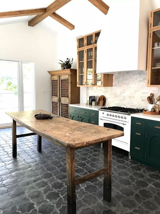 a stylish eclectic kitchen with stained and dark green cabinets, dark grey floor tiles, a vintage wooden kitchen island