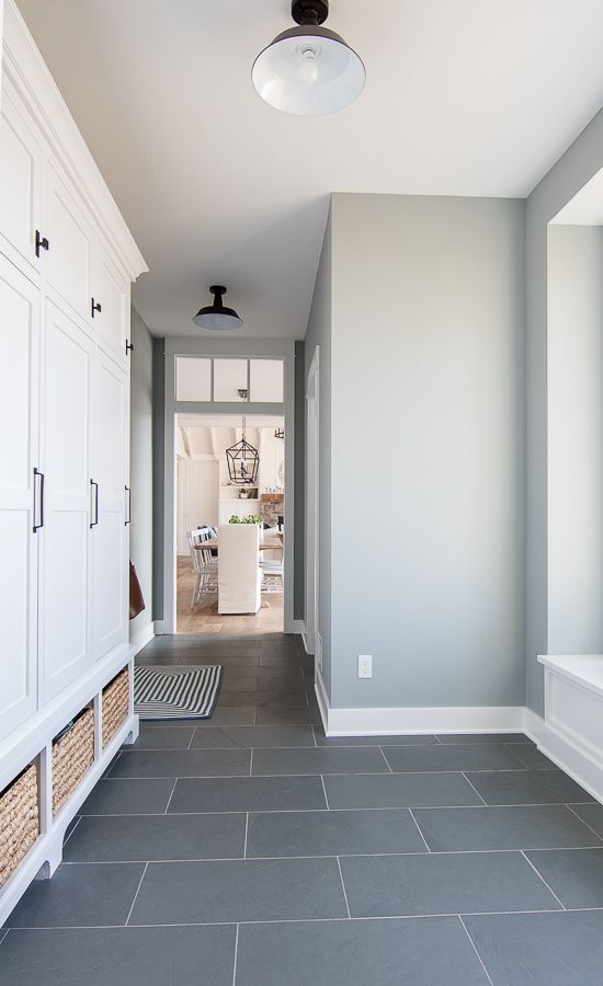 a stylish farmhouse entryway with grey walls and a grey tile floor, white farmhouse storage cabinets and baskets for storage