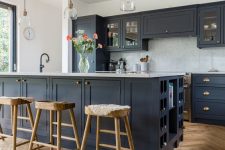 a stylish farmhouse kitchen with light stained parquet flooring, navy cabinets, wooden stools, pendant lamps and brass touches