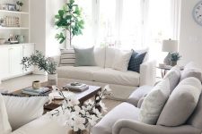 a summer living room in neutrals, with creamy and grey furniture, potted plants, a glass coffee table and some lamps