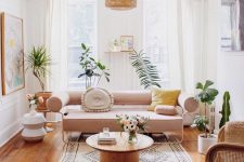 a summer living room with a blush sofa, a rattan chair, bold textiles, a woven lamp and potted plants