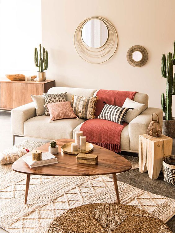 a summer living room with a neutral sofa, a coffee table, printed pillows, potted cacti and a duo of mirrors is warm