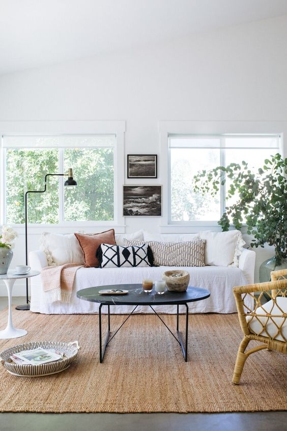 a welcoming summer living room with a white sofa, a black coffee table, printed pillows, black and white artworks and a potted plant